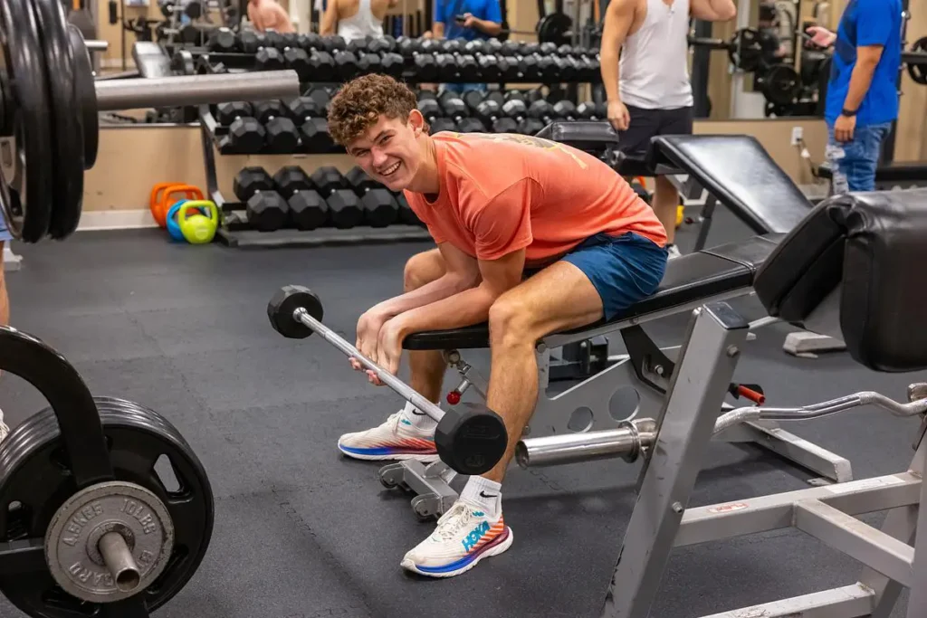 Student lifting weights on a bench in a campus fitness center.