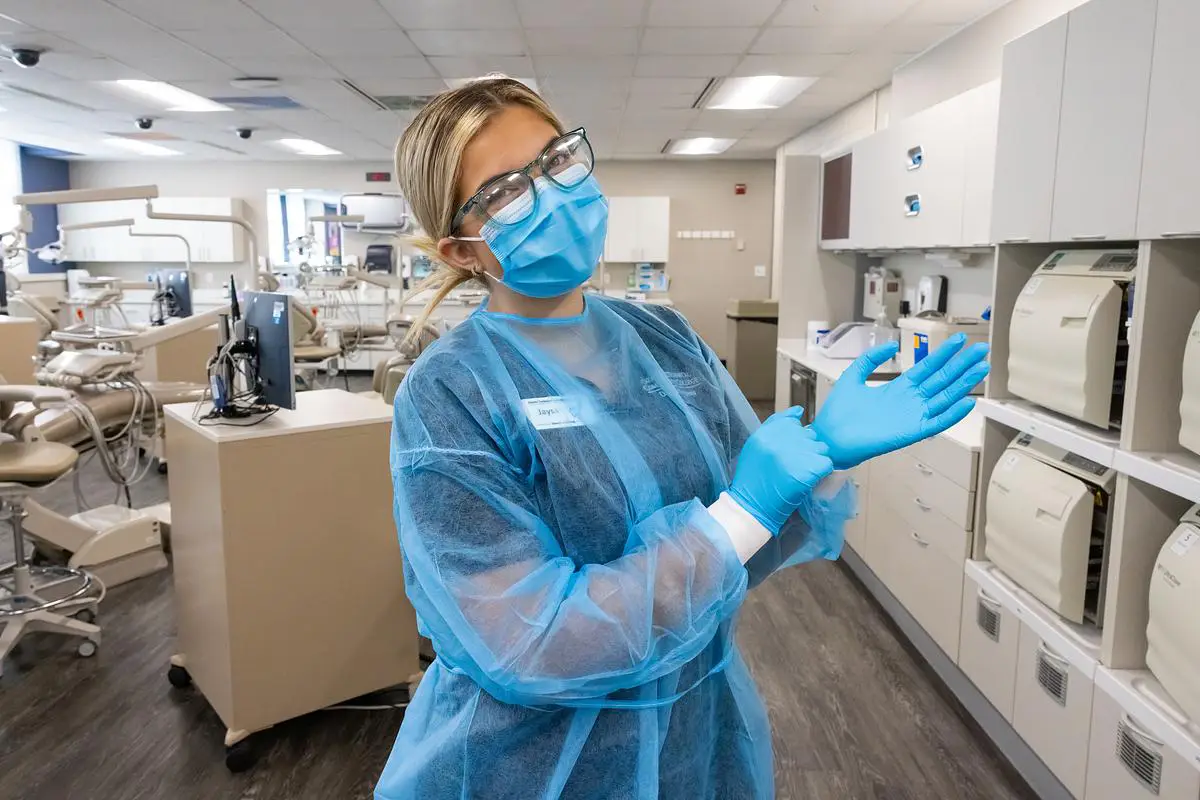 OTC dental student in protective gear putting on gloves in a campus dental lab.