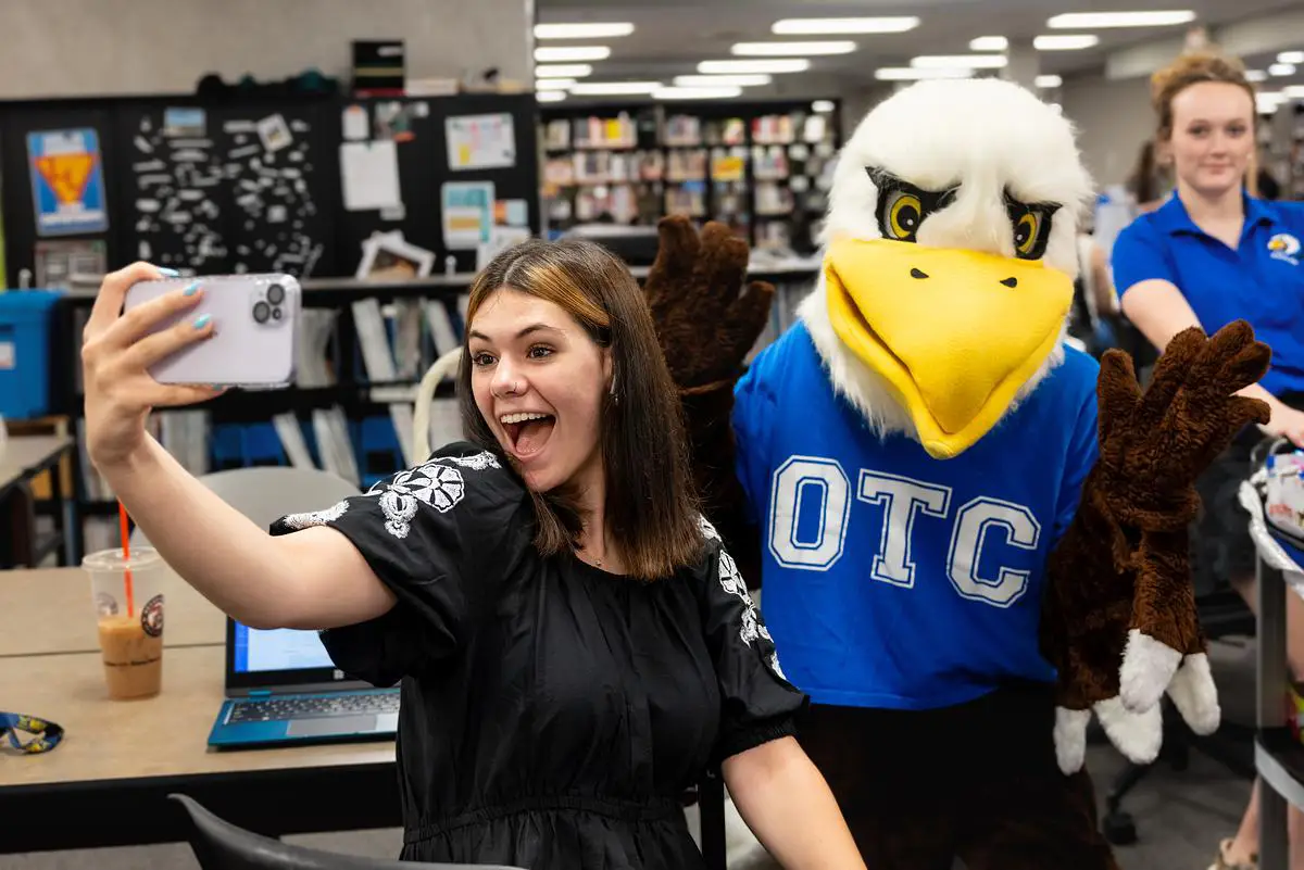 Student takes a selfie with Ozzy the Eagle in the OTC library.