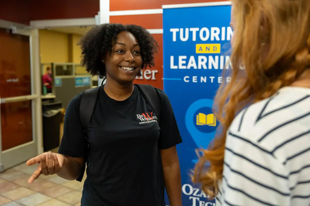A student smiles while talking with another person near the Tutoring and Learning Center sign at Ozarks Technical Community College.