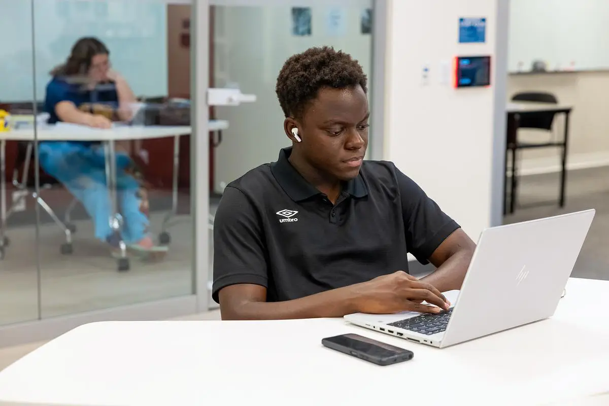 Smiling OTC student standing outside near a brick building and flower bed on campus.