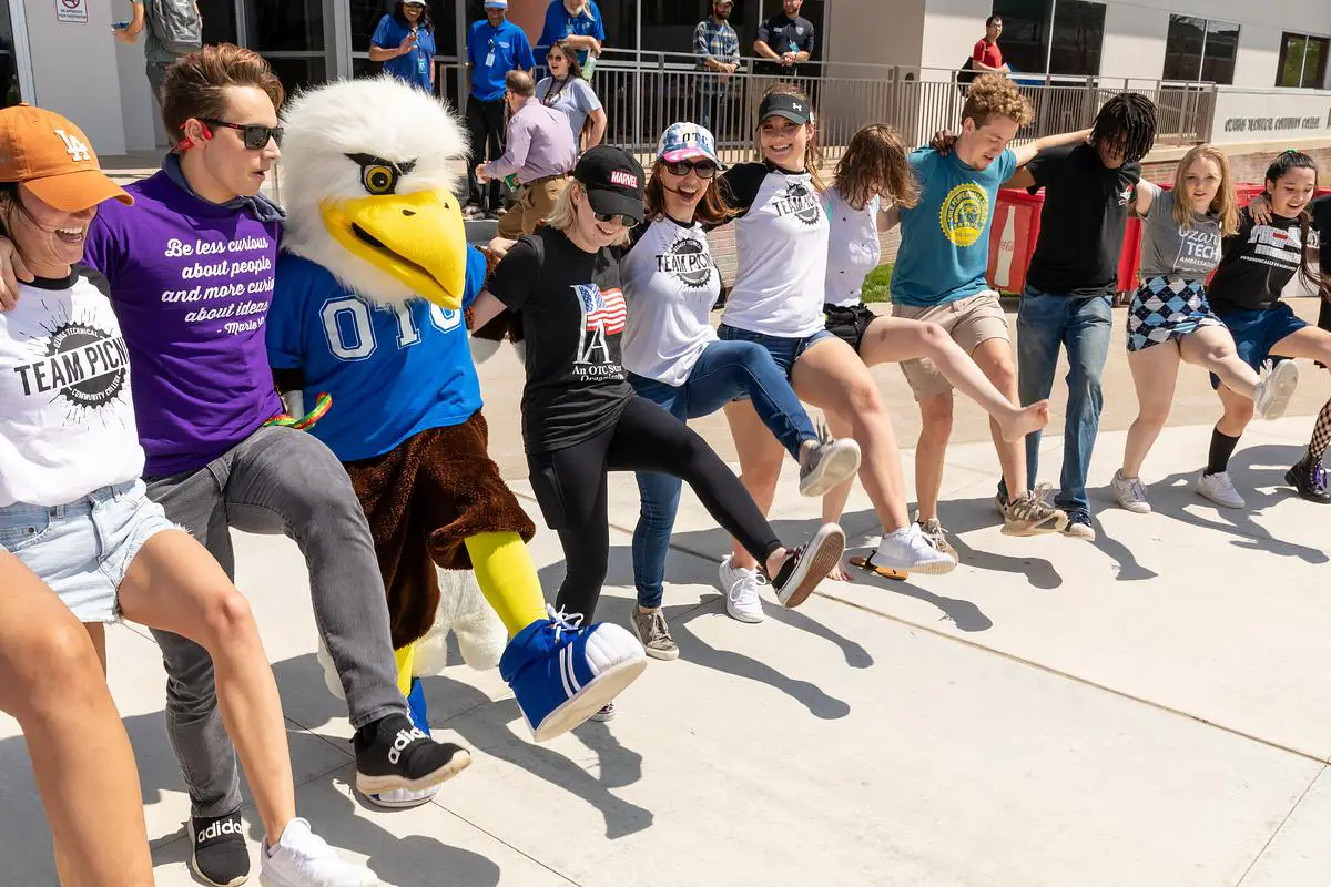 Students link arms and dance with the OTC eagle mascot during a campus event.