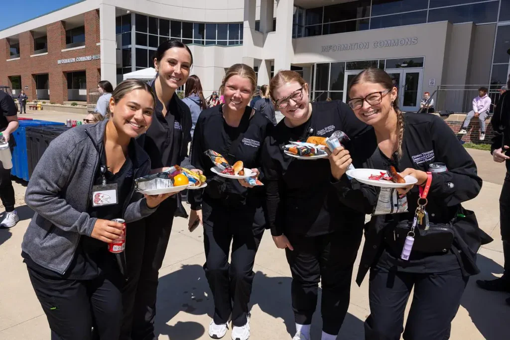 OTC Dental Hygiene students smiling and holding plates of food during the campus picnic outside the Information Commons.