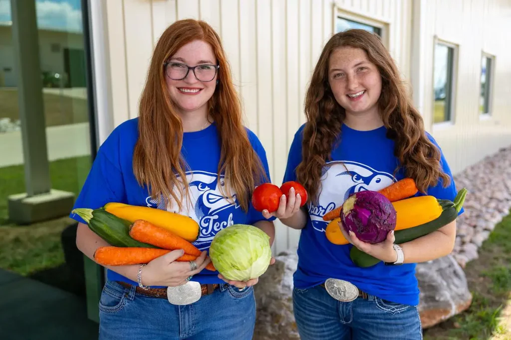 Two OTC students hold fresh vegetables harvested from the Richwood Valley campus garden.