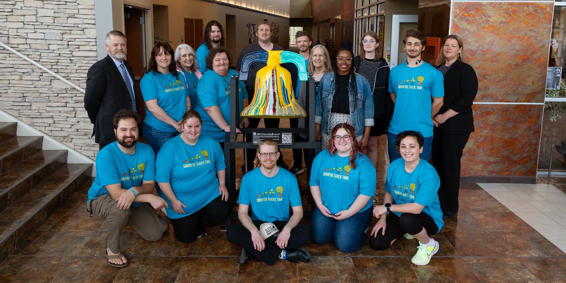 A group is depicted posing around the Be Well Bell