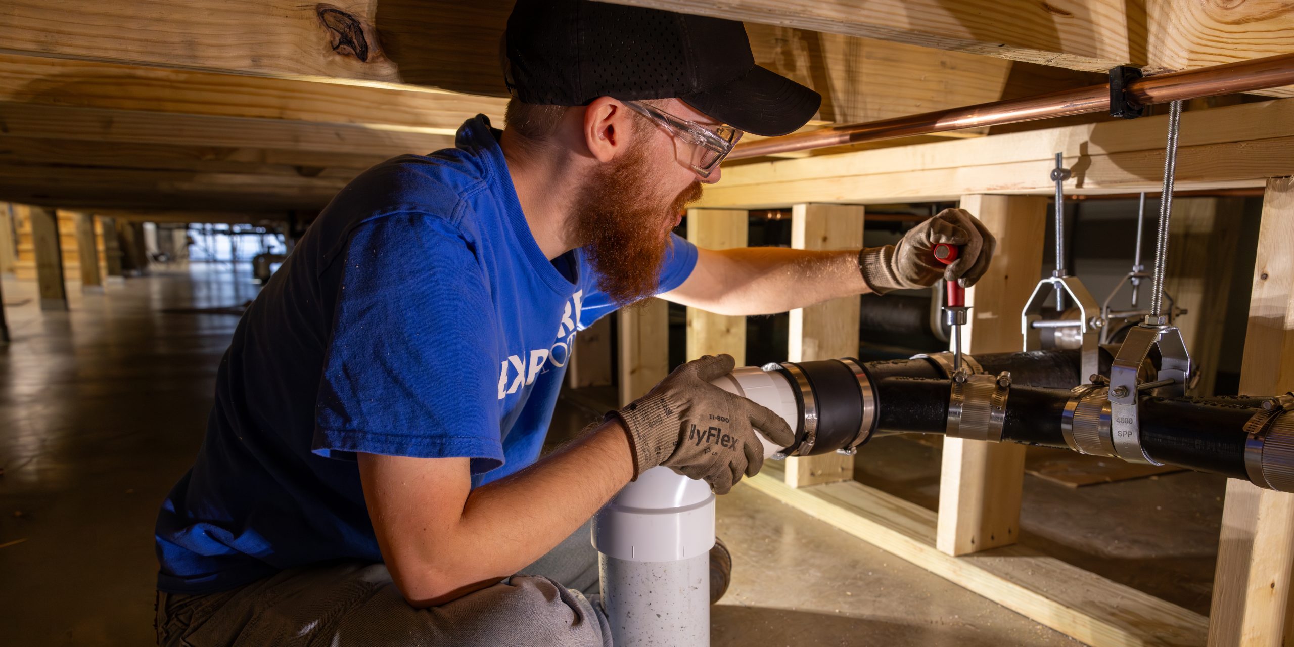 A plumbing student at Ozarks Tech is depicted installing a pipe under a newly constructed building