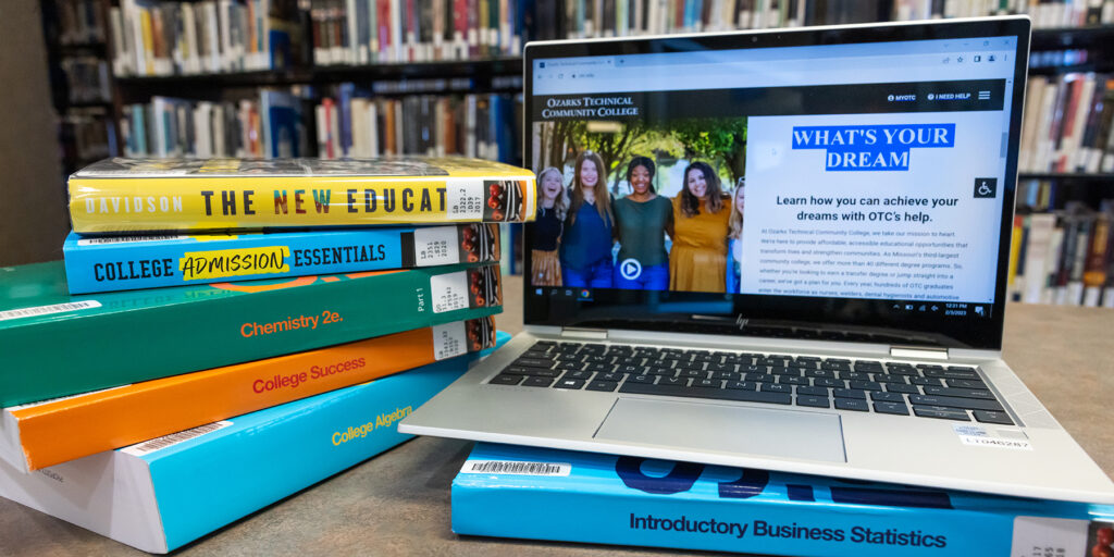 A stack of books and a laptop computer displaying Ozarks Tech's website are depicted on a desk in the Hamra library