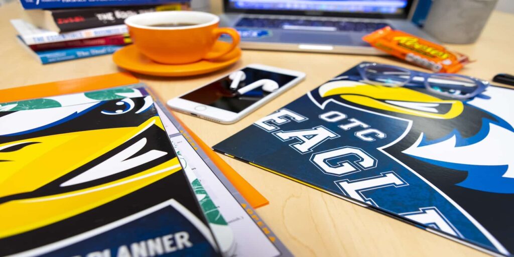 Various magazines, books, and a laptop computer are depicted on a desk