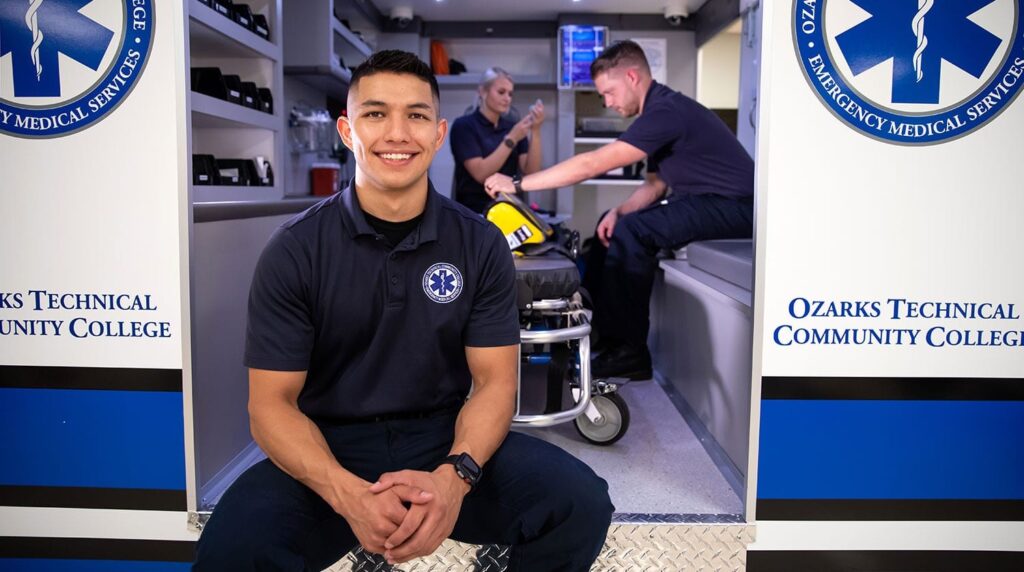 Paramedic sits on the edge of an ambulance as other medical professionals work behind him