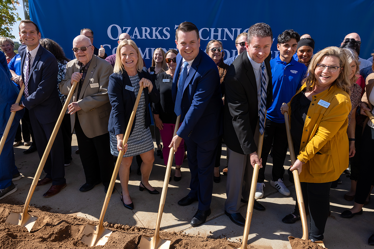 Employees participate in a groundbreaking ceremony, holding shovels and turning soil in front of an Ozarks Tech sign.
