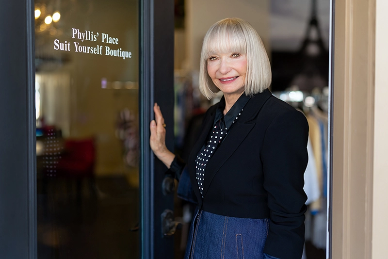 Woman stands in front of a store holding the door open
