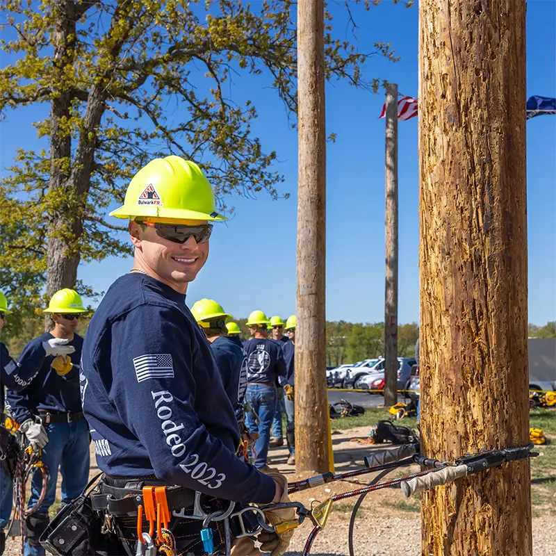 Lineworker in safety gear working beside a utility pole, with crew in background