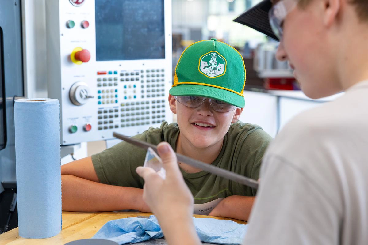 Two students use a file on a part at the manufacturing camp.