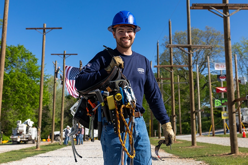 Lineworker poses in front of electrical poles at annual Lineworker Rodeo at Ozarks Tech's Richwood Valley Campus.