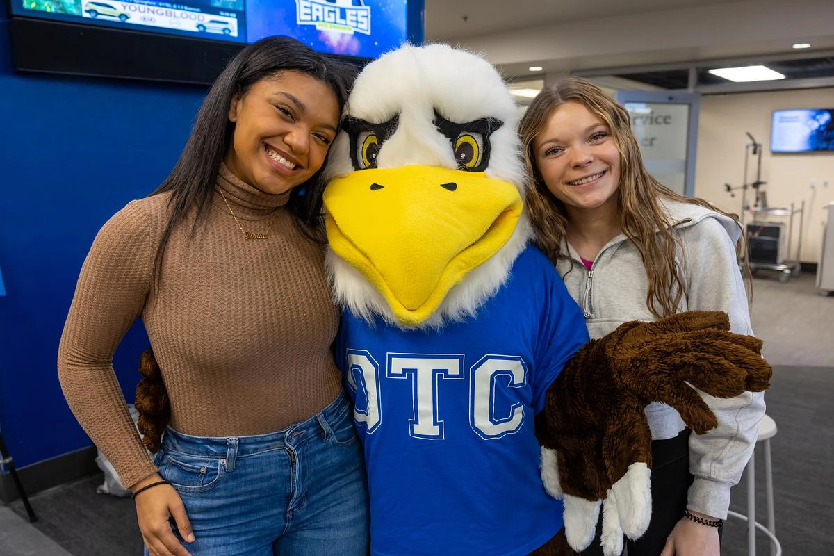 Two students smiling with Ozzy the Eagle mascot.