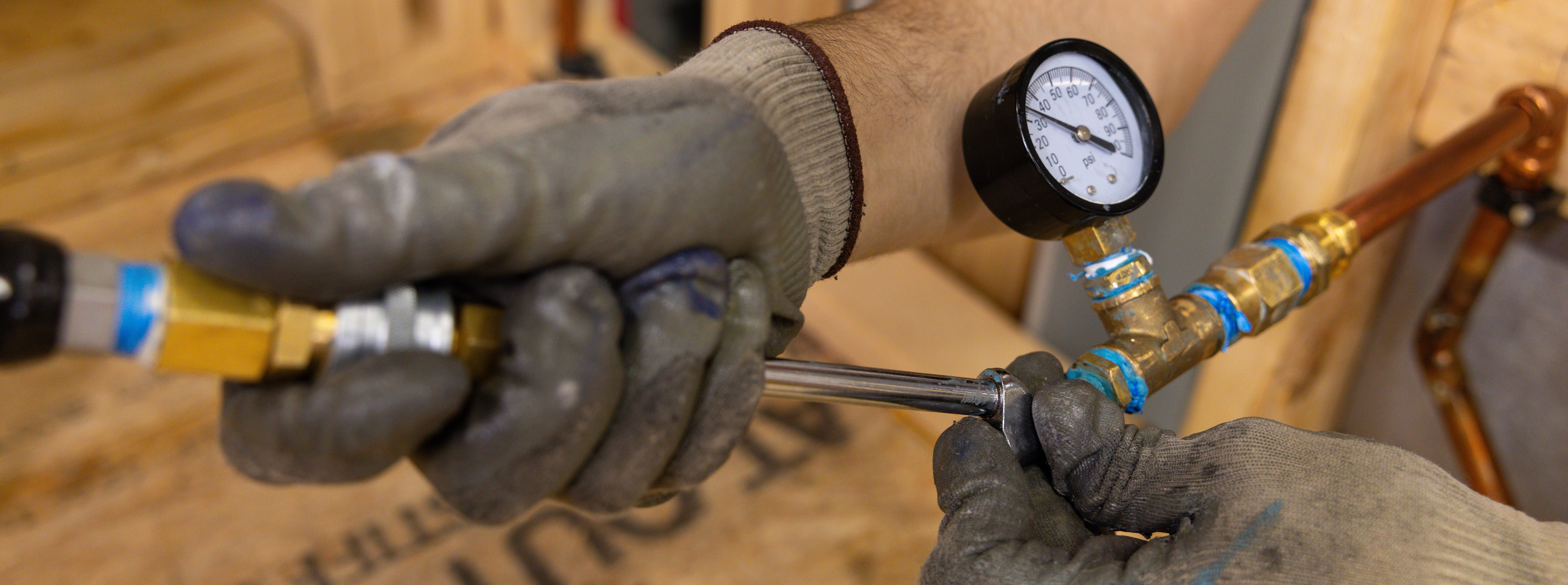 Close up of hands working on a copper pipe with pressure gauge.