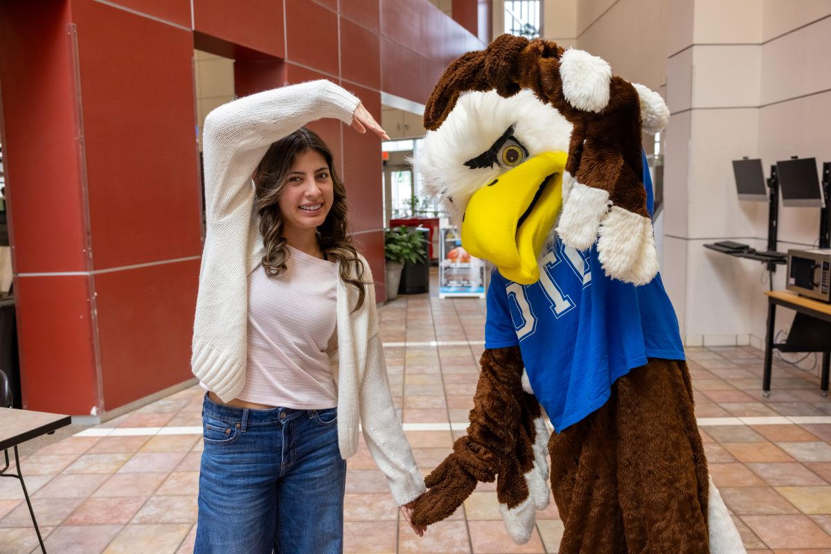 Student and Ozzy the eagle make a heart shape with their arms