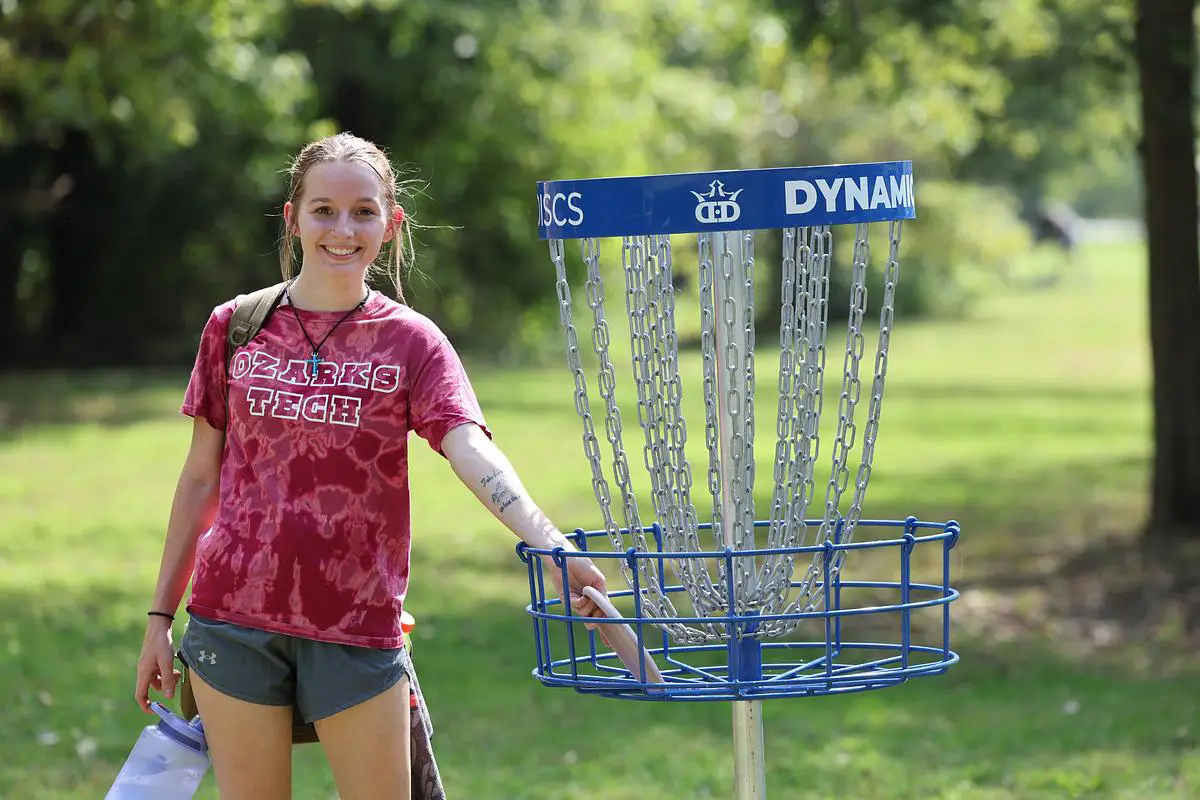 A girl retrieves her disc from the basket on the disc golf course.