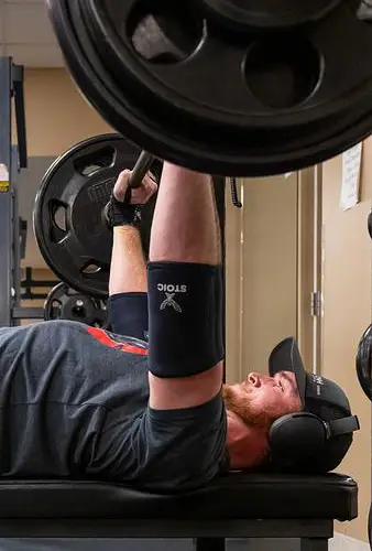 A student holds a barbell above his head while doing a bench press in the gym.