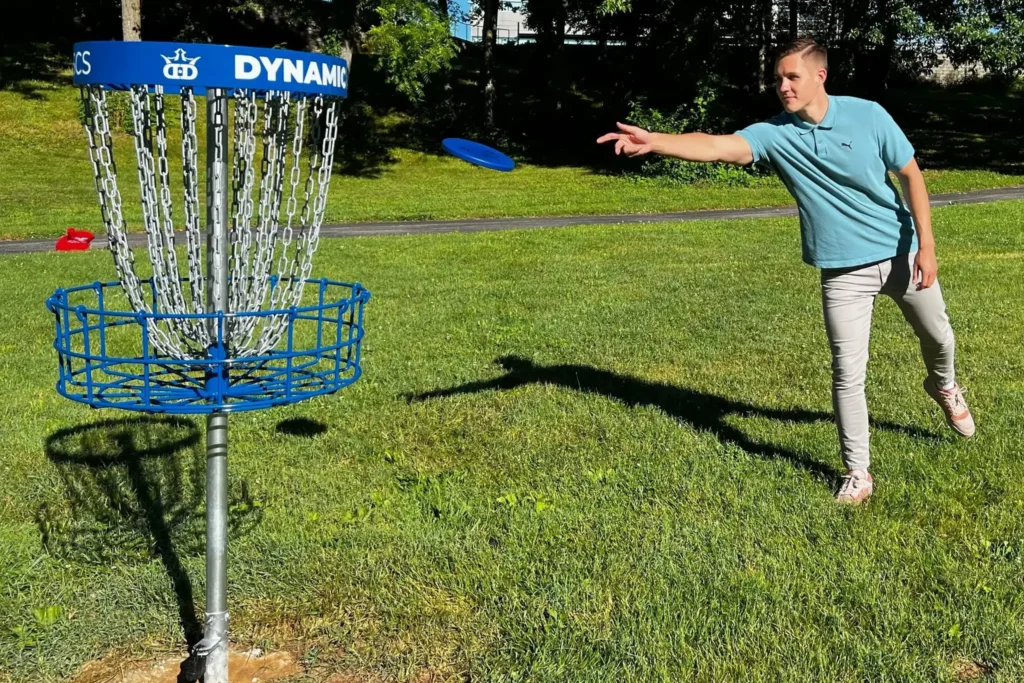 A student throws a disk toward a basket on the disc golf course.