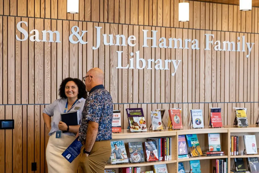 Two people talk in front of a bookshelf in the library.